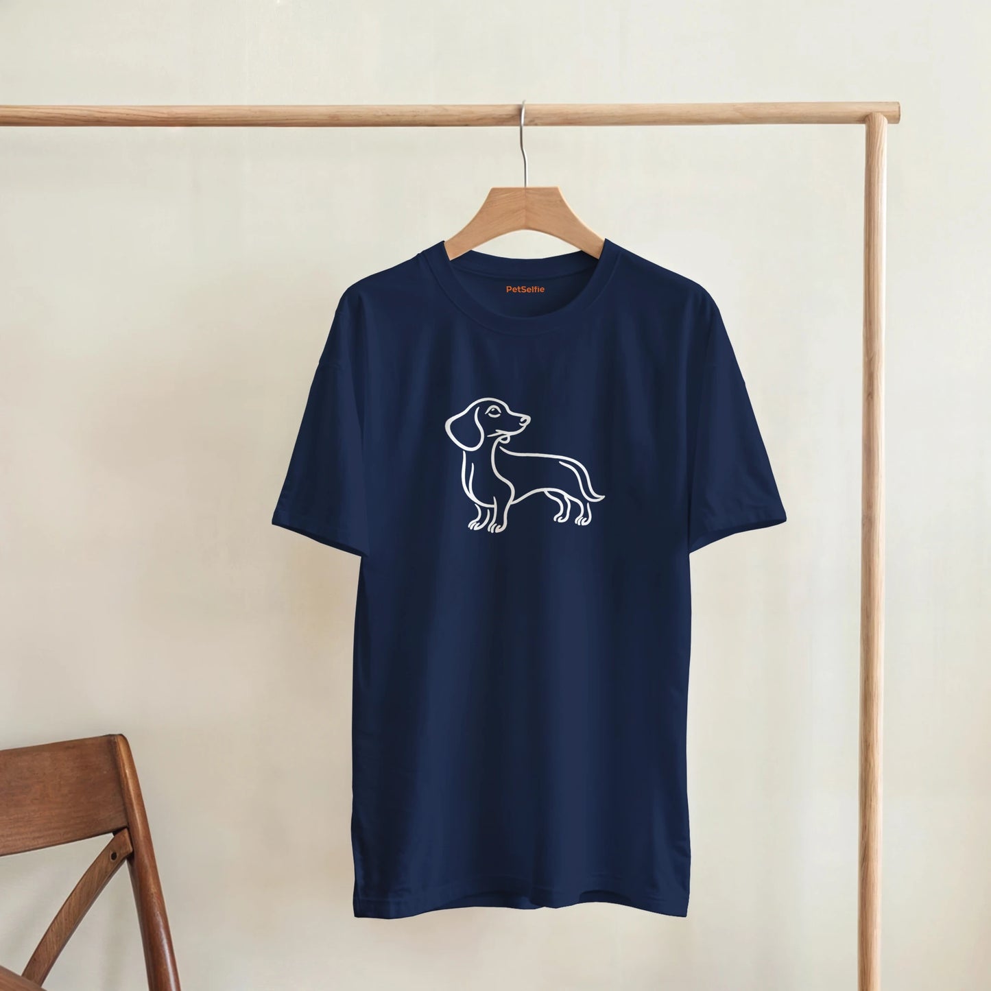 Navy blue t-shirt with a dog graphic on a wooden hanger against a beige wall.