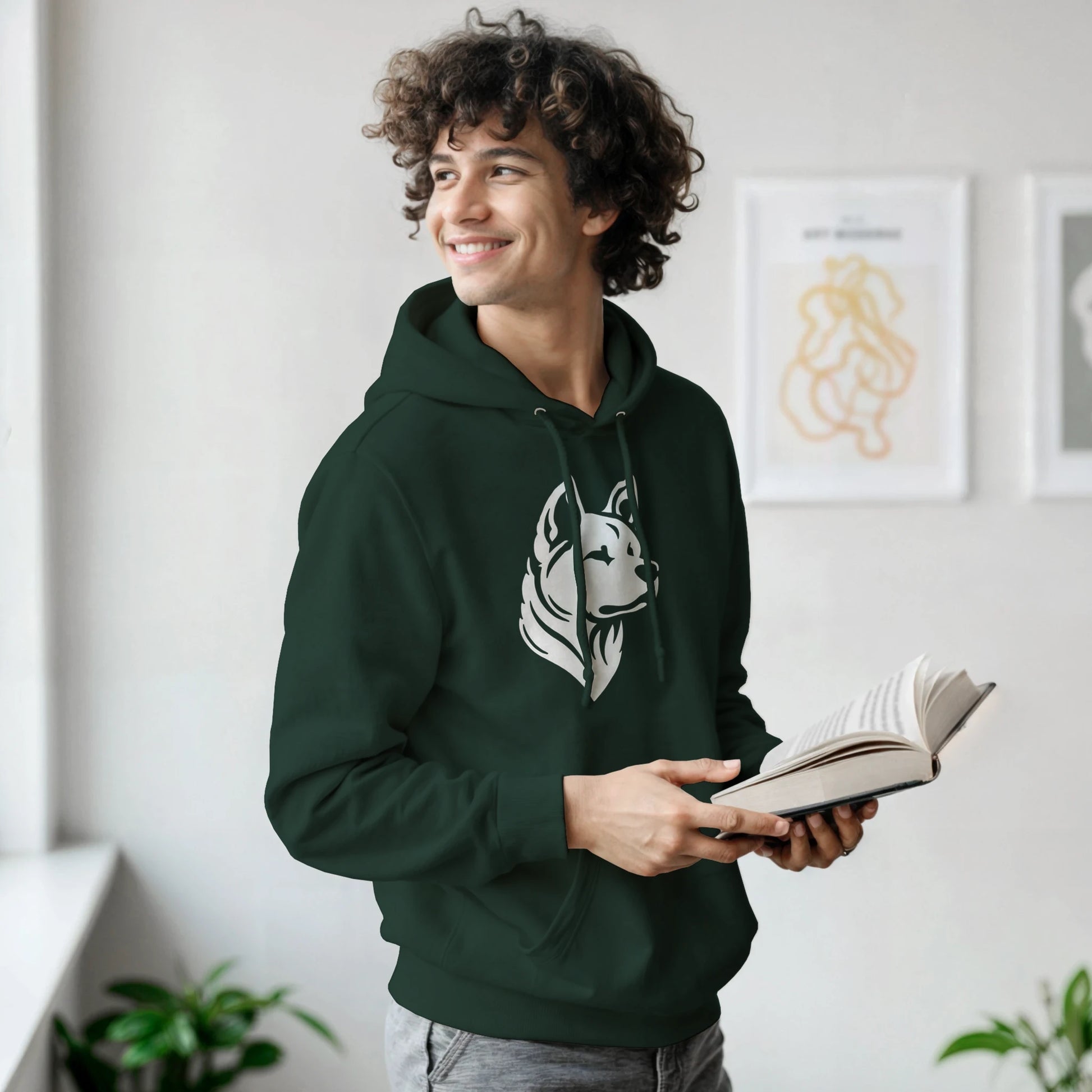 Man wearing a green hoodie with a dog logo, holding a book indoors.