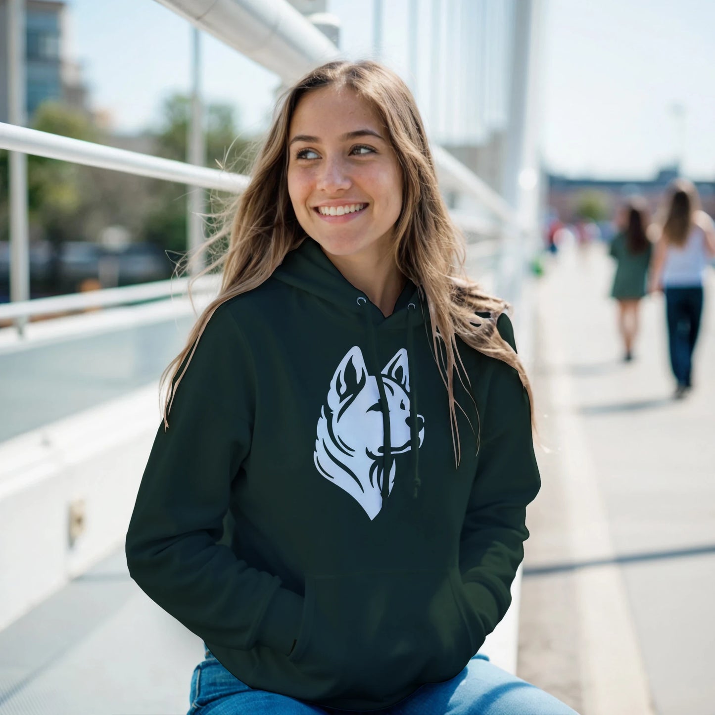 Woman wearing a dark green hoodie with a white dog logo, sitting outdoors on a sunny day.