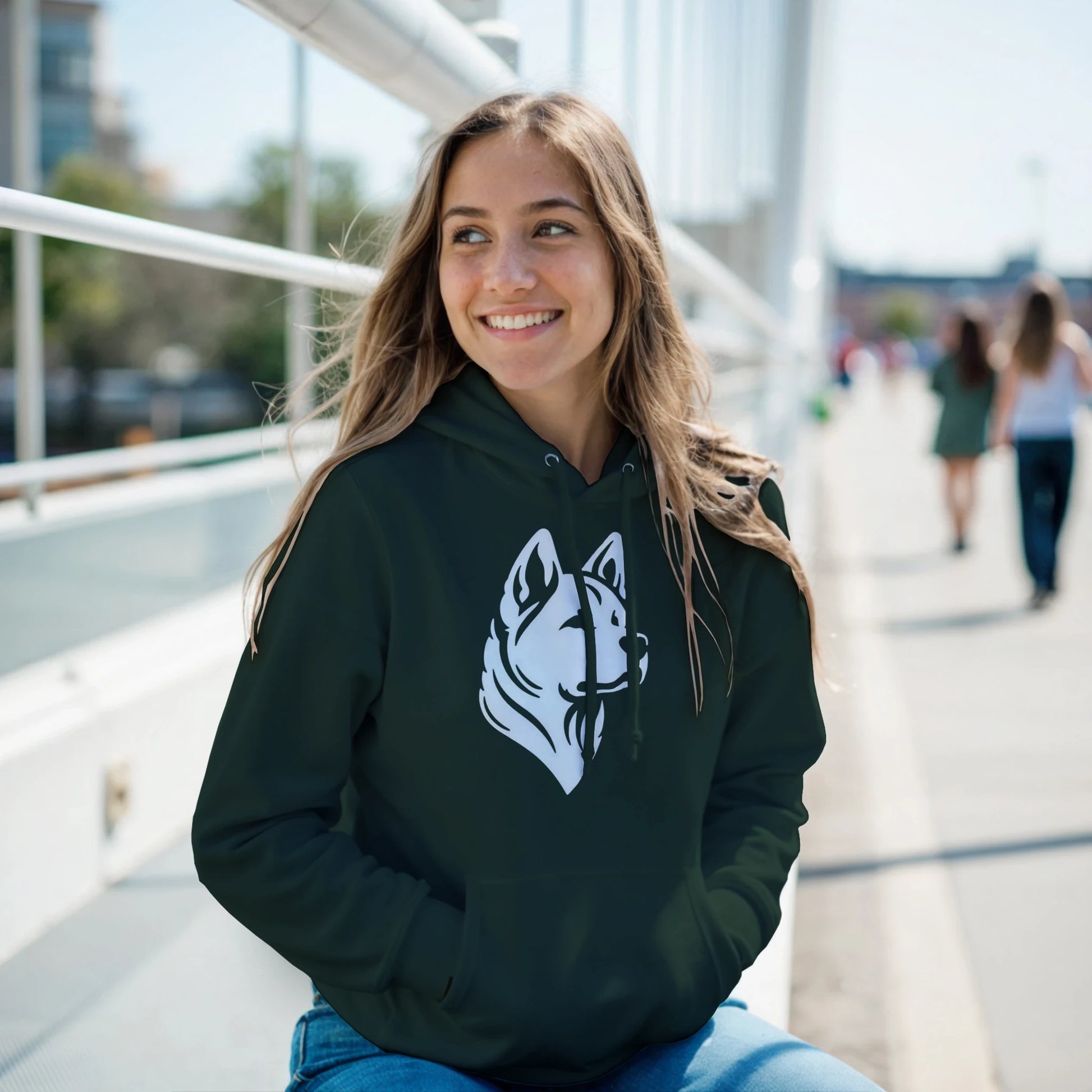 Woman wearing a dark green hoodie with a white dog logo, sitting outdoors on a sunny day.