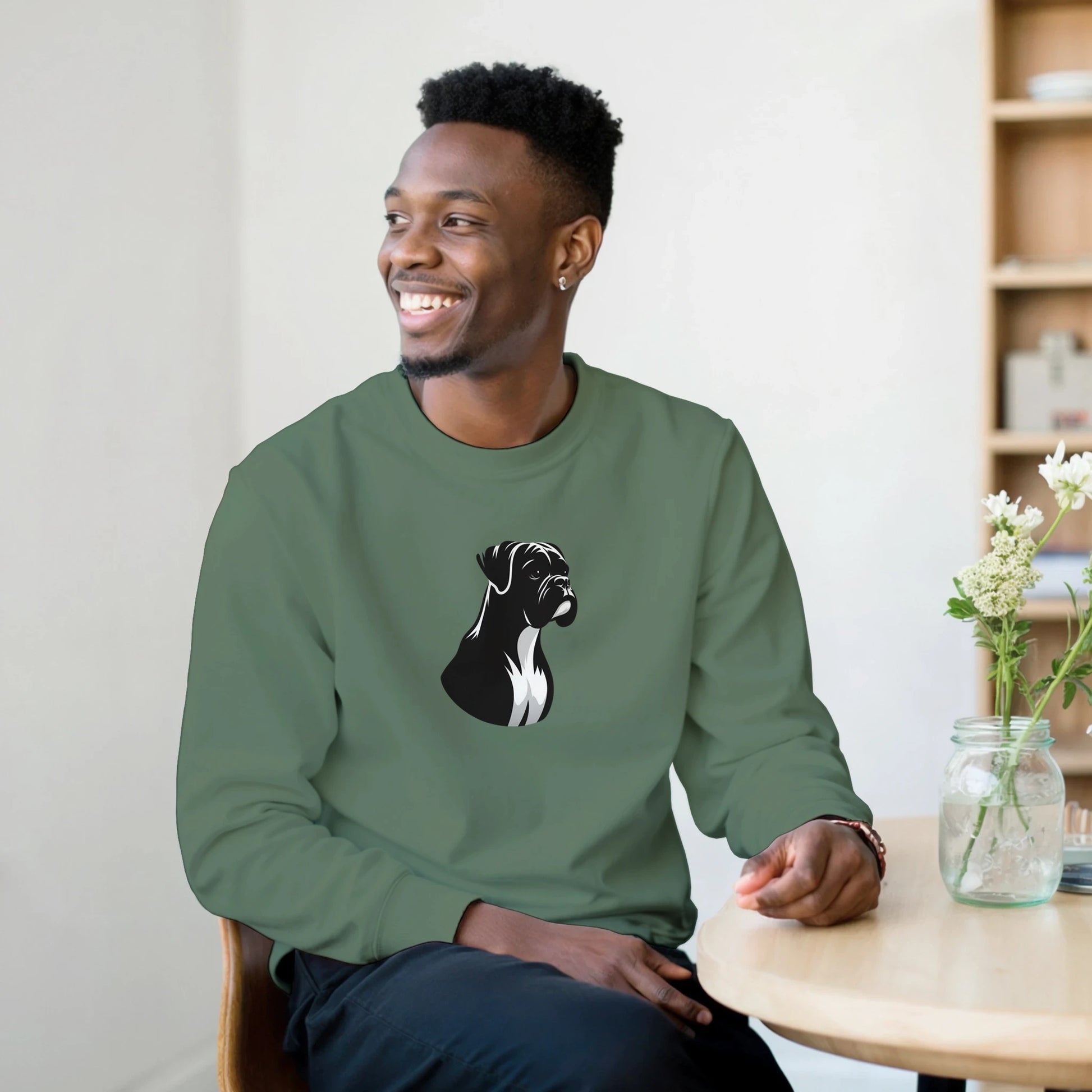 Man wearing a green sweatshirt with a boxer dog graphic, sitting in a room with a table and flowers.