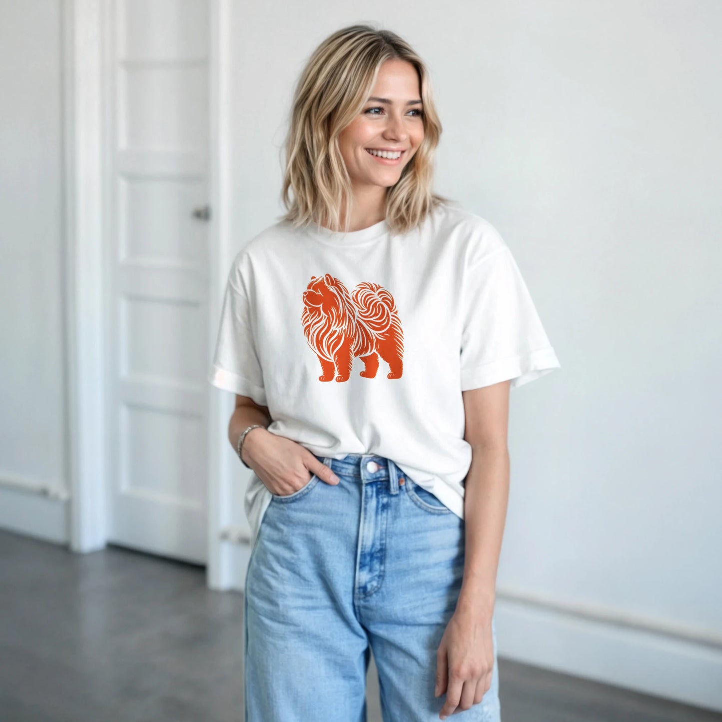 Woman wearing a white t-shirt with an orange chow chow dog graphic and light blue jeans indoors.
