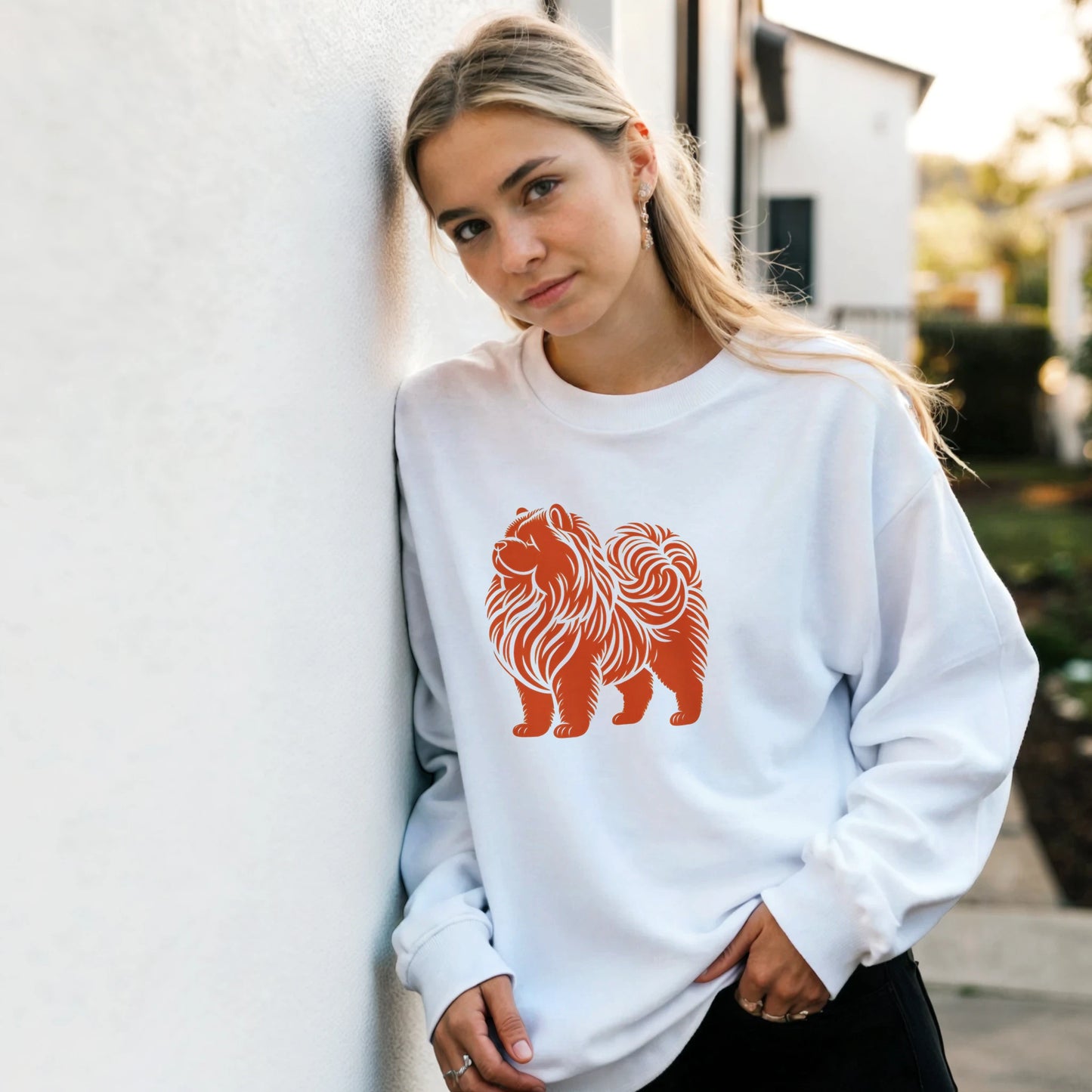 Woman wearing a white sweatshirt with a orange chow chow design outdoors.