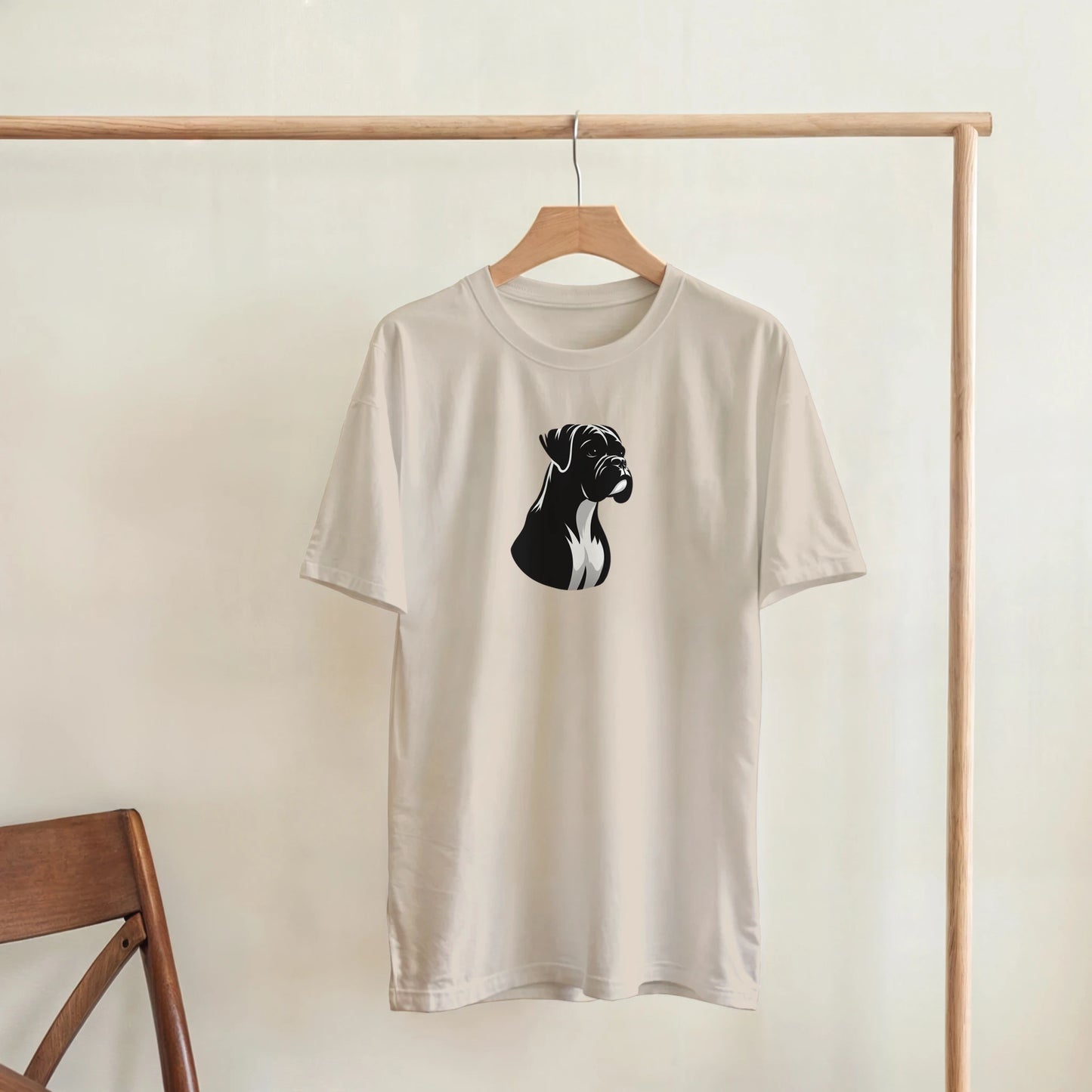 Beige t-shirt with black boxer dog graphic on a wooden hanger against a white wall.